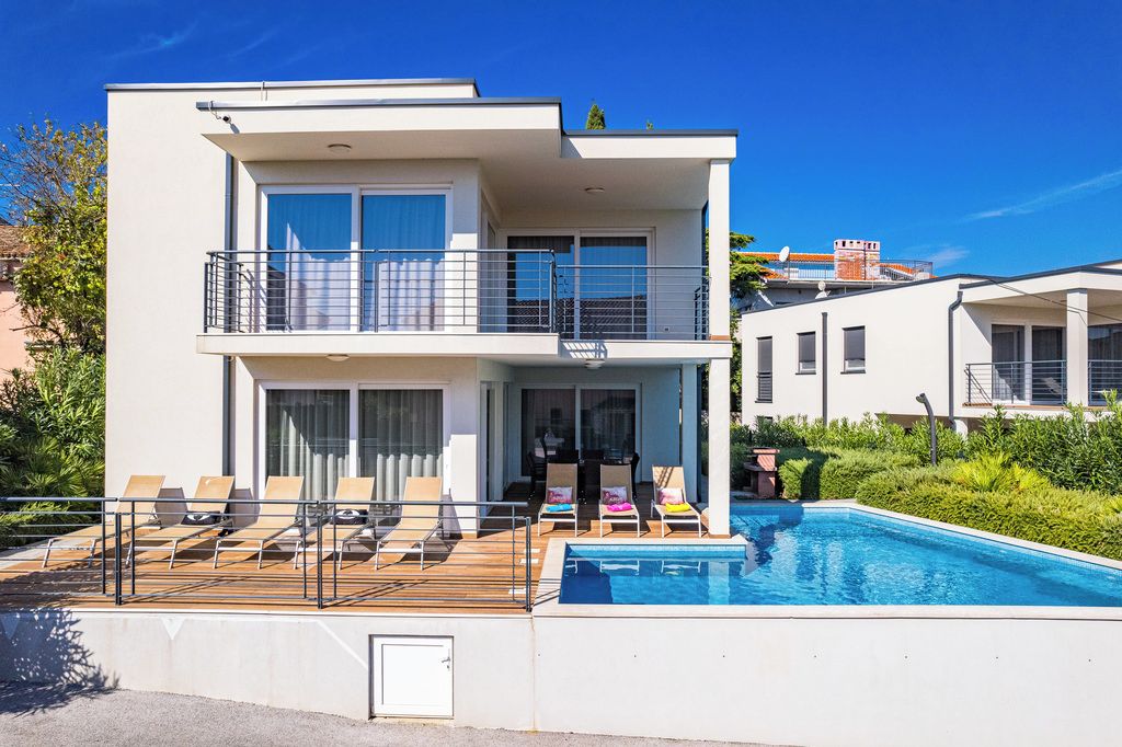 A modern two-story building with a swimming pool, outdoor seating, and a balcony.