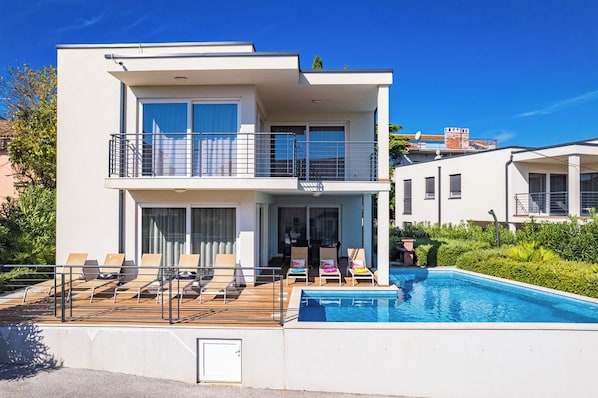 Un bâtiment moderne à deux étages, doté d’une piscine, d’un espace extérieur aménagé et d’un balcon.