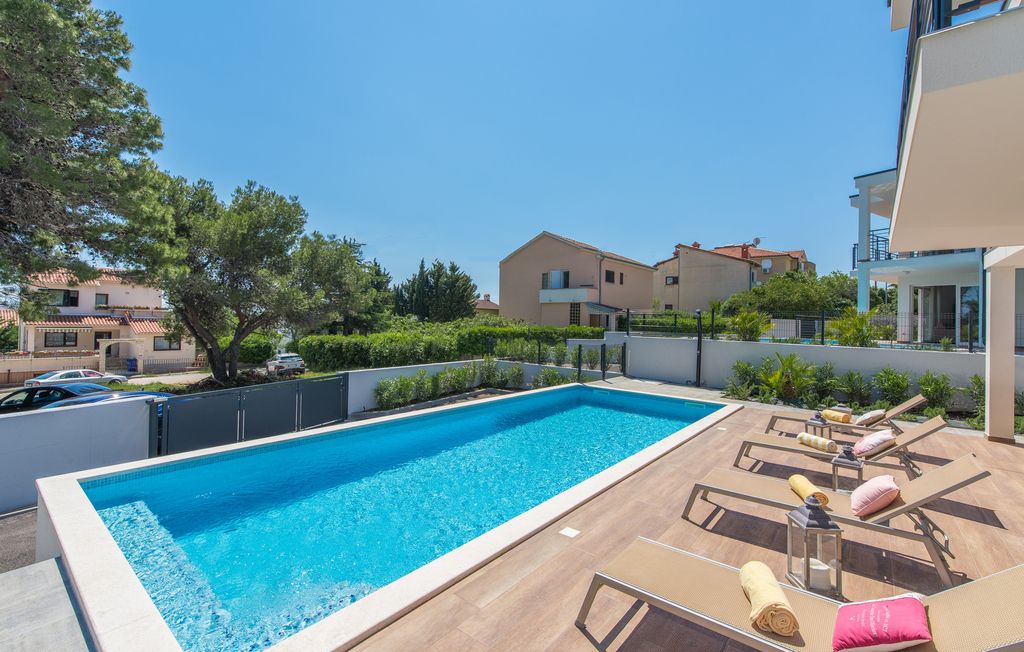 Una piscina rectangular con sillones de descanso y tumbonas, rodeada por una terraza de madera.