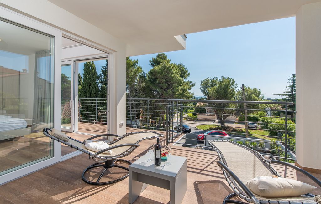 A balcony with a seating area, a table with a bottle and glasses, and a view of the surrounding area.