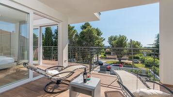 A balcony with a seating area, a table with a bottle and glasses, and a view of the surrounding area.