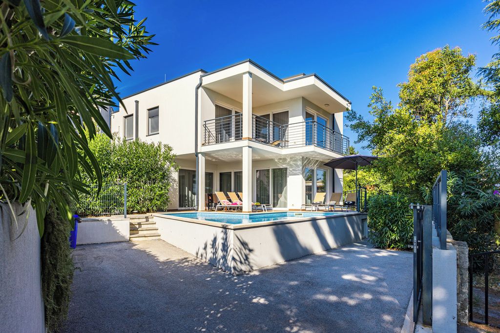 A modern two-story house with a swimming pool, a covered patio, and a garden.
