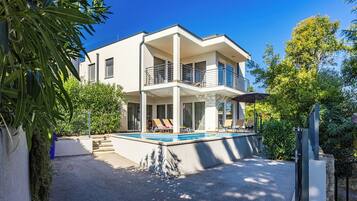 A modern two-story house with a swimming pool, a covered patio, and a garden.