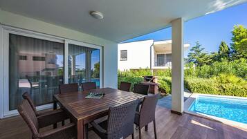 An outdoor patio with a dining table and chairs, a pool, and a view of a modern building.