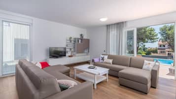 Een moderne woonkamer met een zithoek, een salontafel, een televisie en uitzicht op een zwembad.