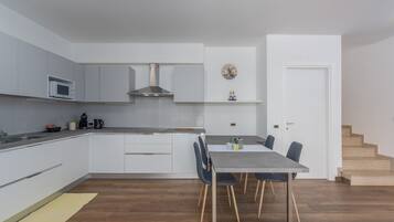 Una cocina moderna con armarios blancos, extractor de acero inoxidable y un comedor con mesa y sillas.