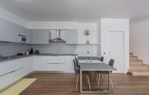 Une cuisine moderne avec des armoires blanches, une hotte en acier inoxydable et un coin repas comprenant une table et des chaises.