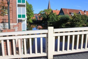 A wooden bridge with railings, a river, and buildings with red roofs and a church spire in the background. - Holiday apartment with 1 bedroom (Otterndorf)