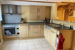 A kitchen with a built-in oven, a stovetop, a sink, and wooden cabinets. - Holiday apartment with 1 bedroom (Otterndorf)