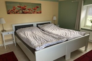 Een bed met een wit frame en bloemenbeddengoed, een nachtkastje met een lamp, en een bloemschilderij aan de muur.