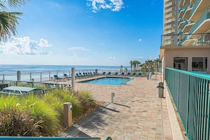 A pool area with a view of the ocean, lounge chairs, and a building with balconies. - #1607 Twin Towers 2/2 Oceanfront Condo (Daytona Beach Shores)