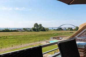 A balcony with a view of a grassy field, a swimming pool, and a bridge in the distance. - Holiday apartment Sundseele DG (Fehmarn)