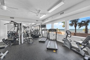 Ein Fitnessstudio mit Laufbändern, Kraftgeräten und einem Fernsehbildschirm mit Blick auf einen Strand.