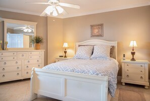 Ein Schlafzimmer mit Bett, Nachttischen, einer Kommode, Deckenventilator, Spiegel und einem gerahmten Bild an der Wand.