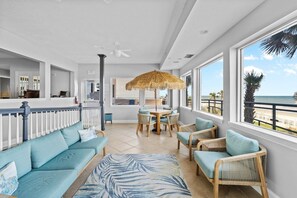 A spacious indoor area with a dining table and chairs, a sofa, and a large window offering a view of the beach. - Spacious Oversized Balcony on 2nd Floor - Great Ocean Views (Daytona Beach Shores)