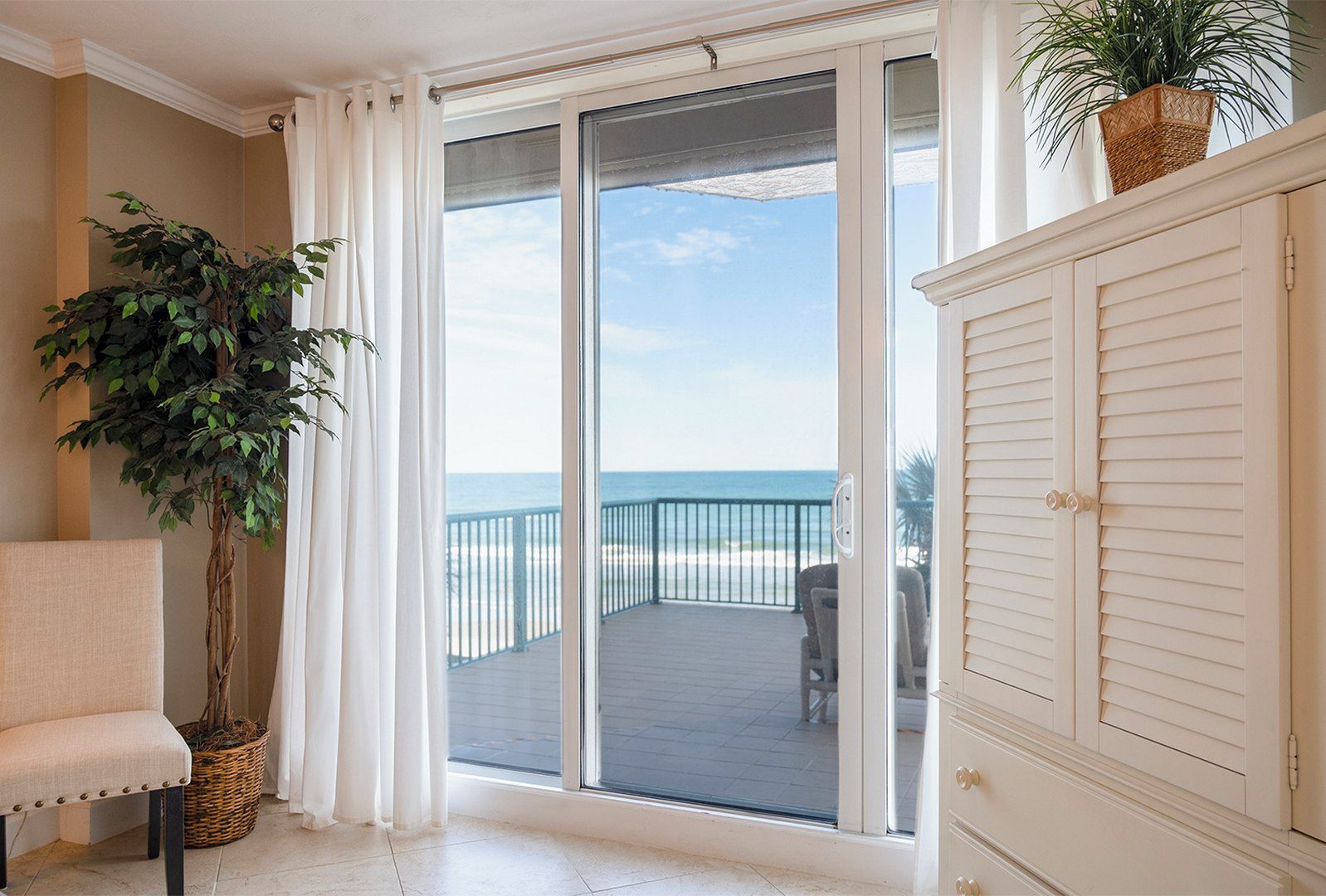 A room with a view of the ocean, a balcony with a chair, and a cabinet.