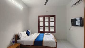 Ein Schlafzimmer mit einem Bett, einem Nachttisch, einem an der Wand montierten Fernseher, einem Deckenventilator und einem Fenster mit Jalousien.