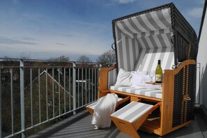 A wicker chair with a striped cushion and a bottle of wine on a balcony with a railing. - Holiday apartment with 2 bedrooms (Scharbeutz)