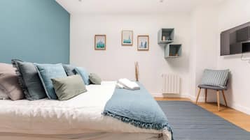 Une chambre à coucher comprenant un lit, des oreillers, une table de chevet, une chaise, un radiateur et des étagères fixées au mur.
