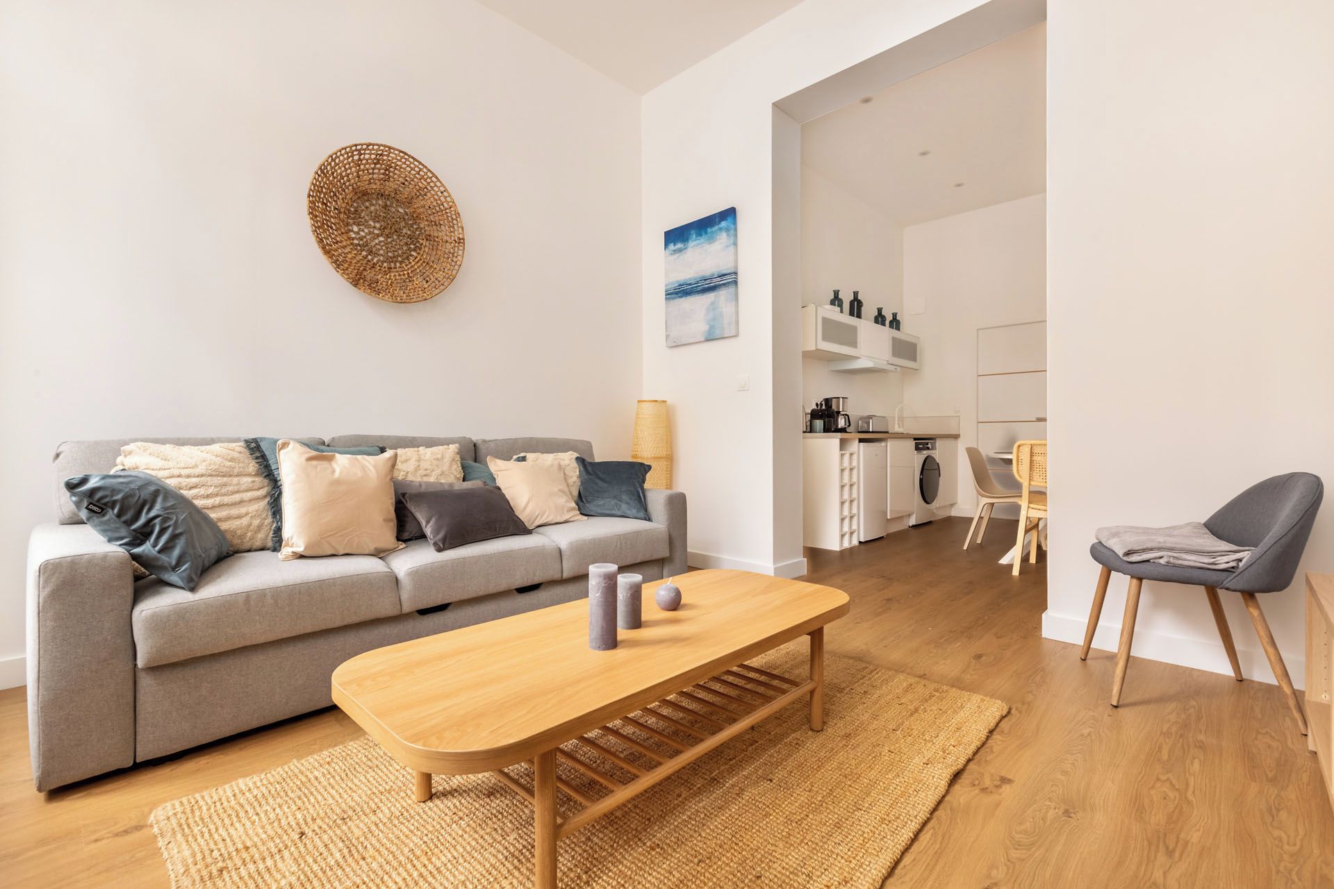 Ein modernes Wohnzimmer mit einem grauen Sofa, einem Holztisch und einer Küche im Hintergrund.