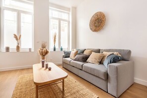 Ett modernt vardagsrum med en grå soffa, ett soffbord i trä och en vävd matta.