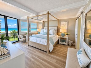 A four-poster bed with a view of the ocean, a balcony with a chair, and a bedside table with a lamp. - Lighthouse Shores Condo 105 (Ponce Inlet)