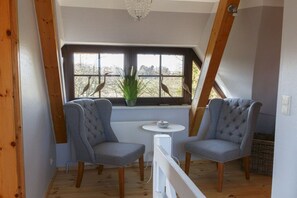 A room with two upholstered chairs, a small round table, and a window with a view of trees. - Holiday home with 3 bedrooms (Born a. Darß)