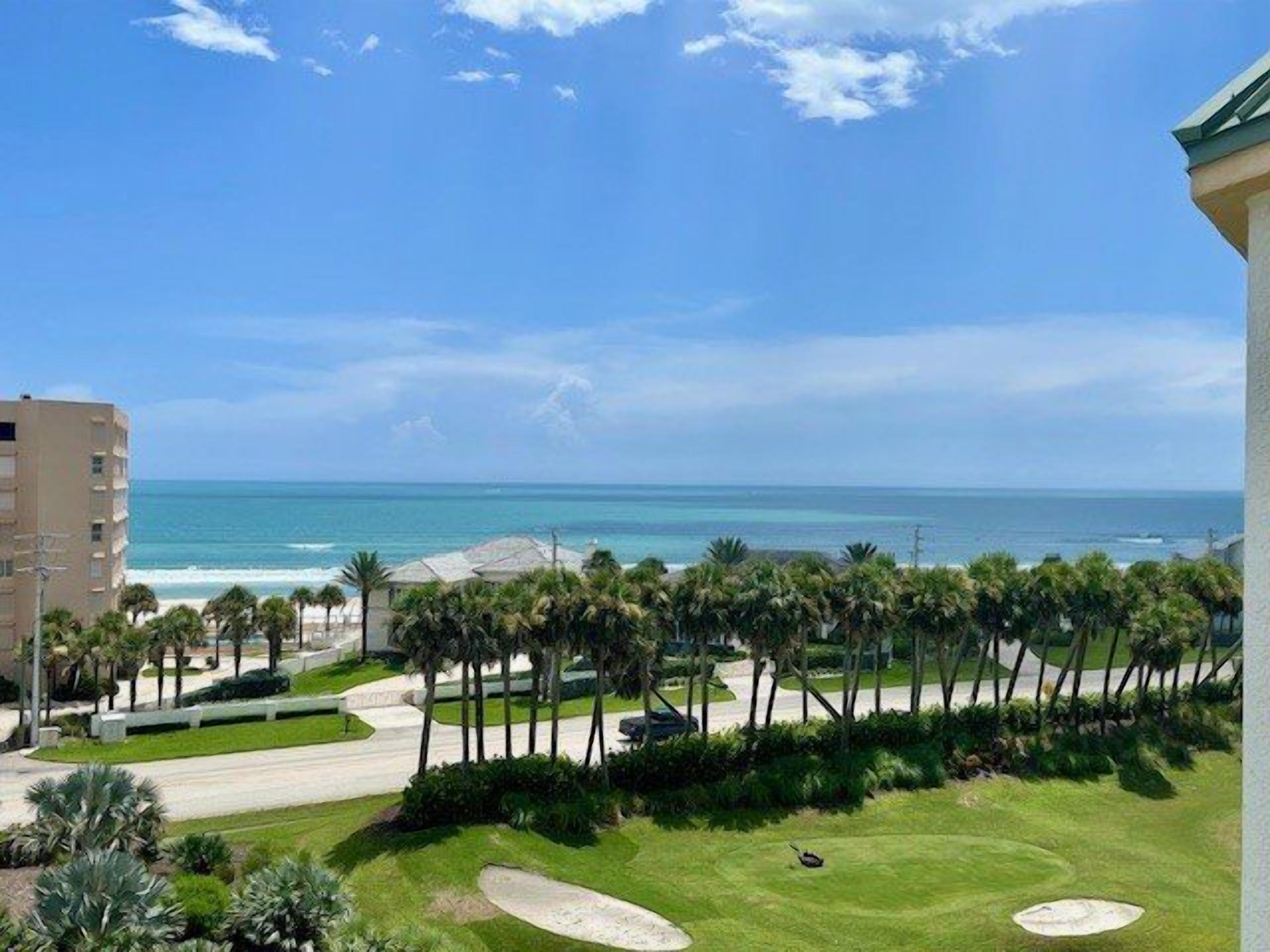 A view of a coastal area with a road, palm trees, and a building.
