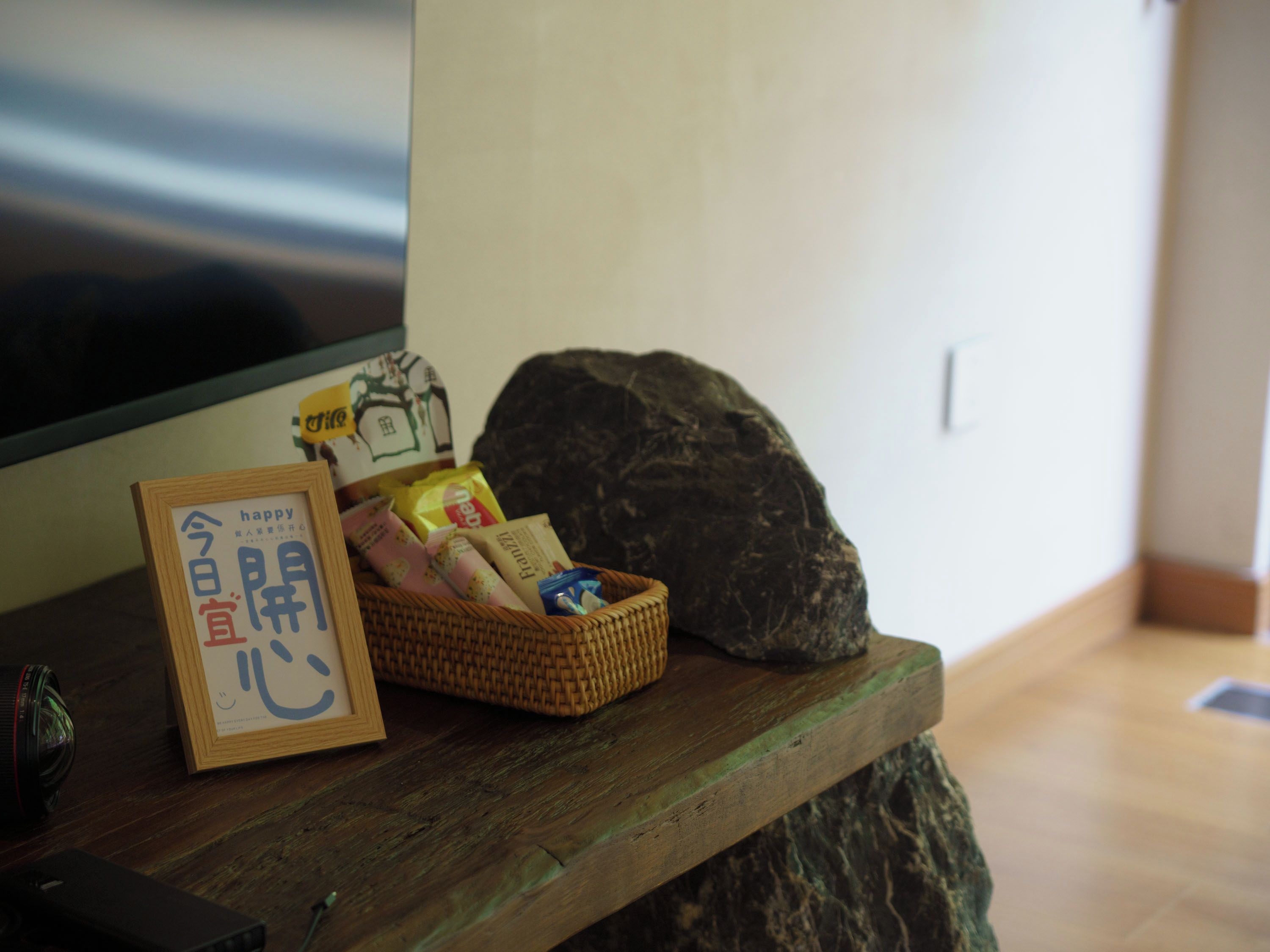 A wooden table with a framed sign, a wicker basket with snacks, and a large rock.