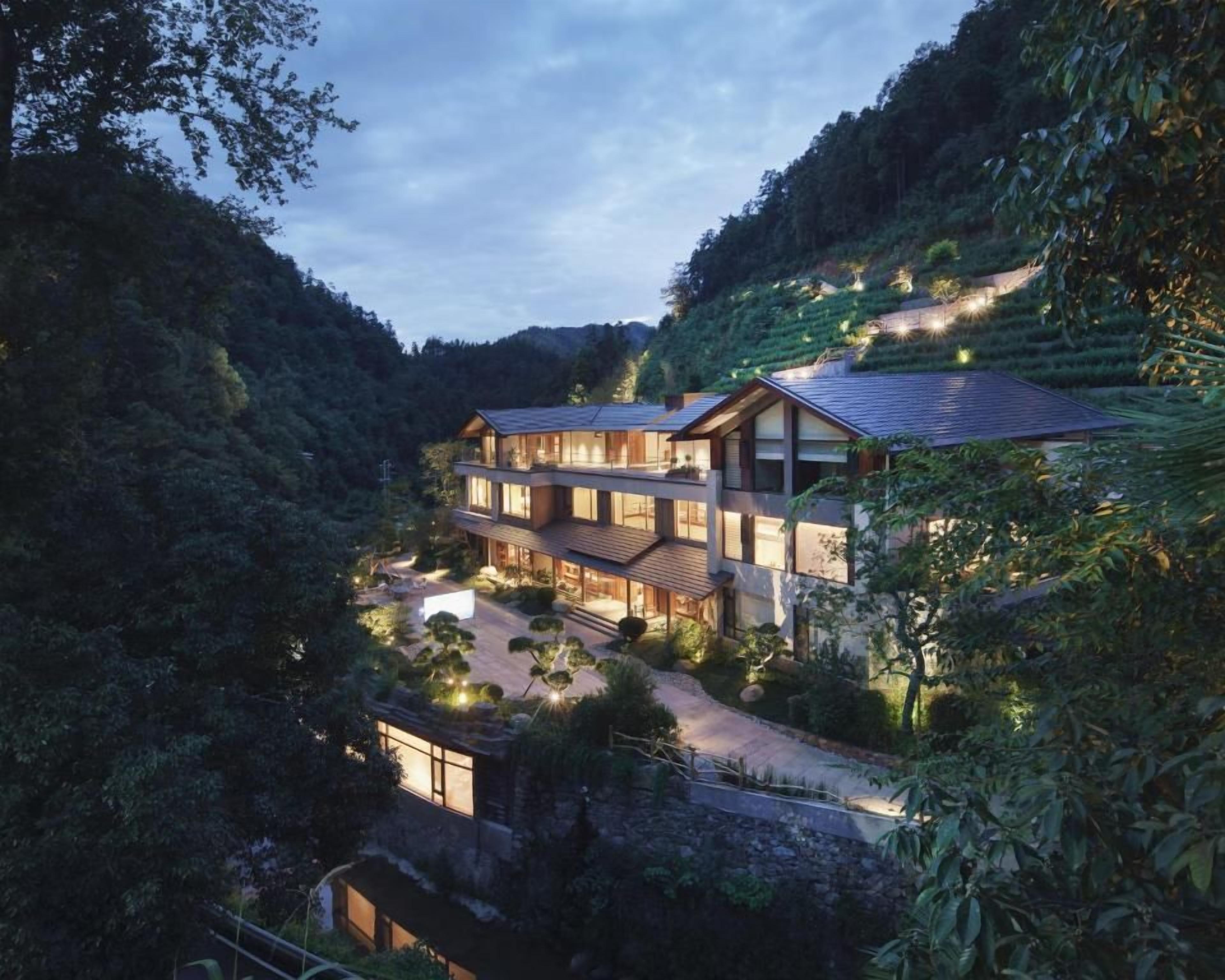 A multi-story building with a modern design, surrounded by lush greenery and terraced fields.