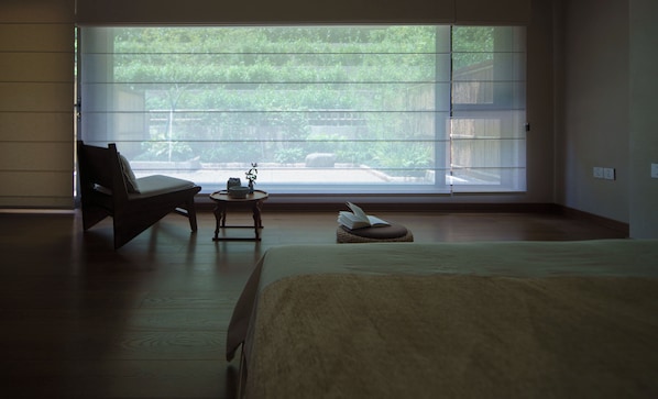 A bedroom with a large window, a bed, a chair, and a small table with a plant.