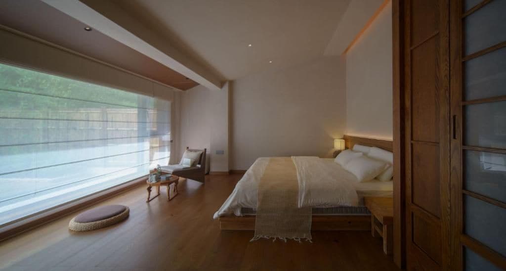 A bedroom with a bed, bedside table, and a window with blinds.