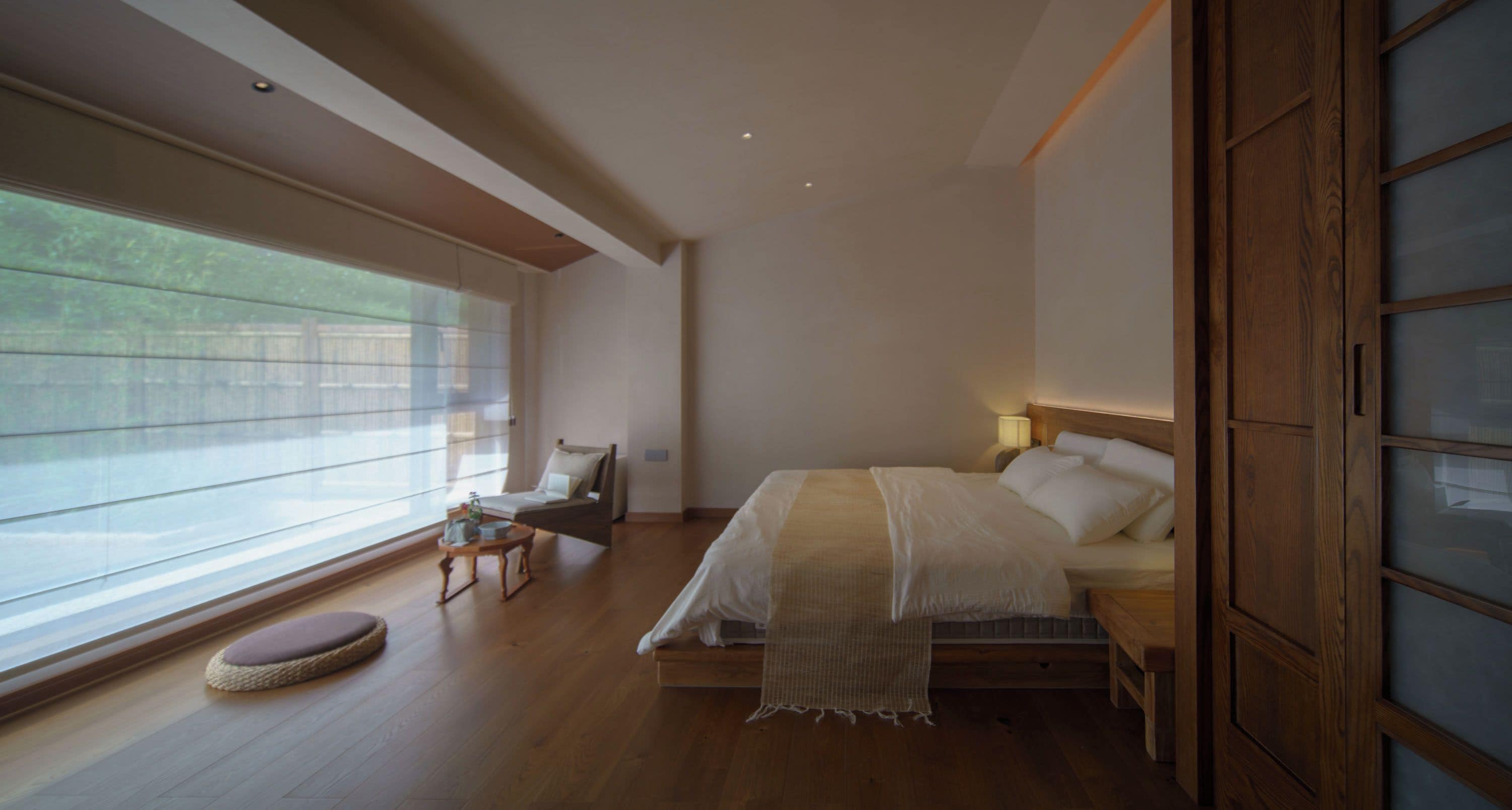 A bedroom with a large bed, a bedside table, a chair, and a window with blinds.
