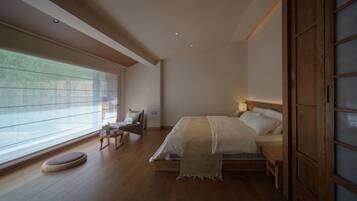 A bedroom with a large bed, a bedside table, a chair, and a window with blinds.