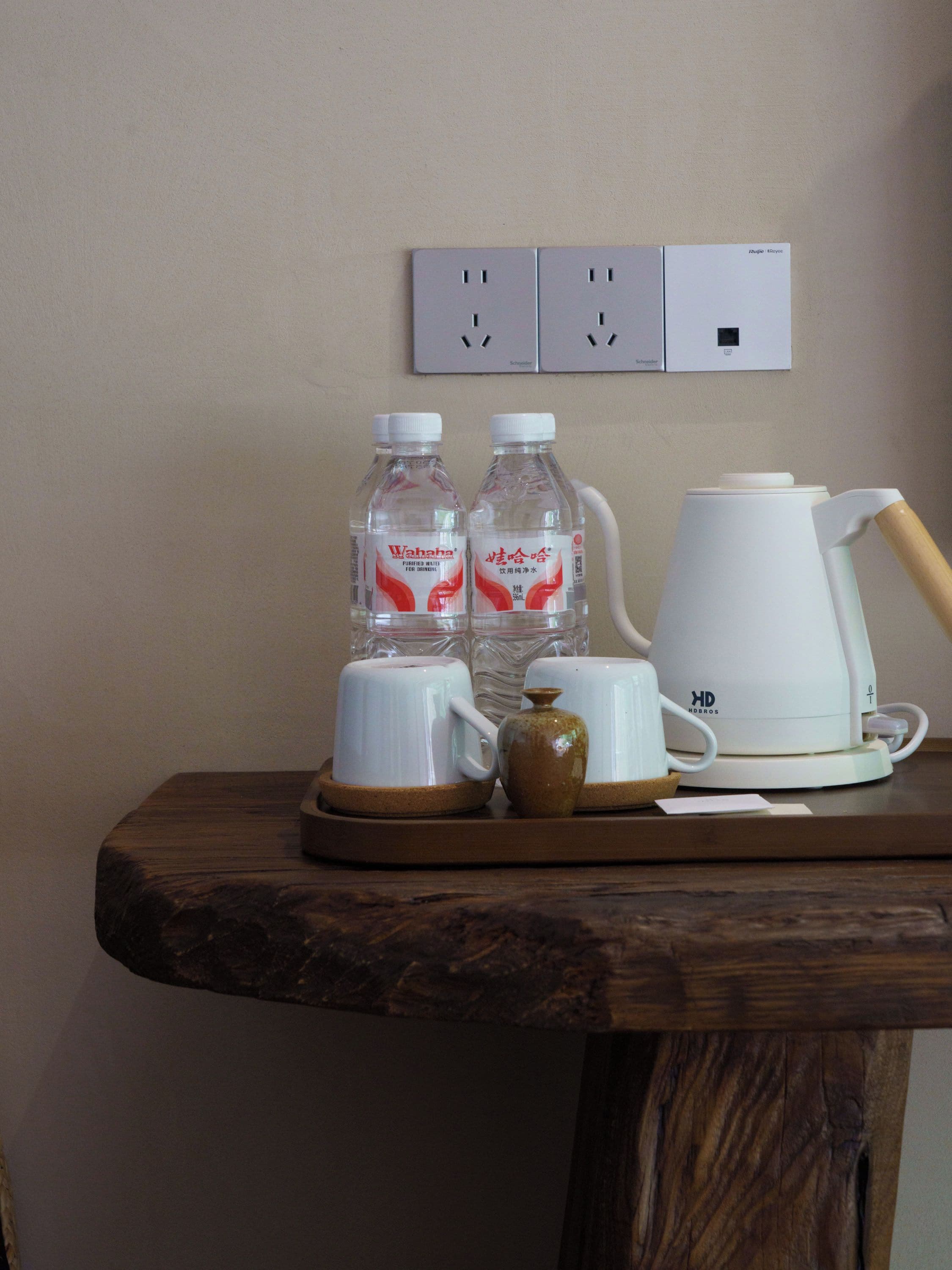 Una mesa de madera con una cafetera blanca, dos botellas de agua y una taza de cerámica.