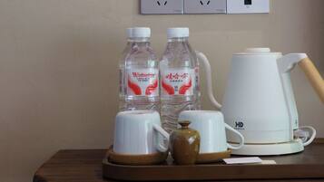 Una mesa de madera con una cafetera blanca, dos botellas de agua y una taza de cerámica.