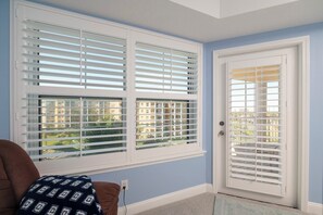 A room with a door and windows with white blinds, a brown chair, and a patterned throw blanket. - Links at Harbor Village D505 (Ponce Inlet)