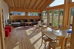 A wooden interior with a sofa, chairs, a dining table, and large windows. - Golden Timber Lodge – Exklusives Ferienhaus in Selchow (Selchow)