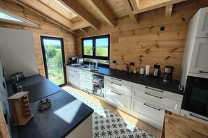 A compact kitchen with wooden walls, a black countertop, and a built-in dishwasher. - Golden Timber Lodge – Exklusives Ferienhaus in Selchow (Selchow)
