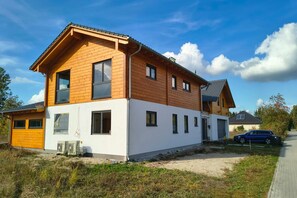 A two-story house with a white lower floor and a wooden upper floor, featuring multiple windows and a garage. - Golden Timber Lodge – Exklusives Ferienhaus in Selchow (Selchow)