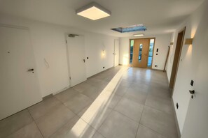 A long, narrow hallway with white walls, a tiled floor, and doors on both sides. There is a door at the end with a glass panel. - Golden Timber Lodge – Exklusives Ferienhaus in Selchow (Selchow)