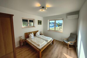 A bedroom with a wooden bed, a window with a view, a chair, and a ceiling light fixture. - Golden Timber Lodge – Exklusives Ferienhaus in Selchow (Selchow)