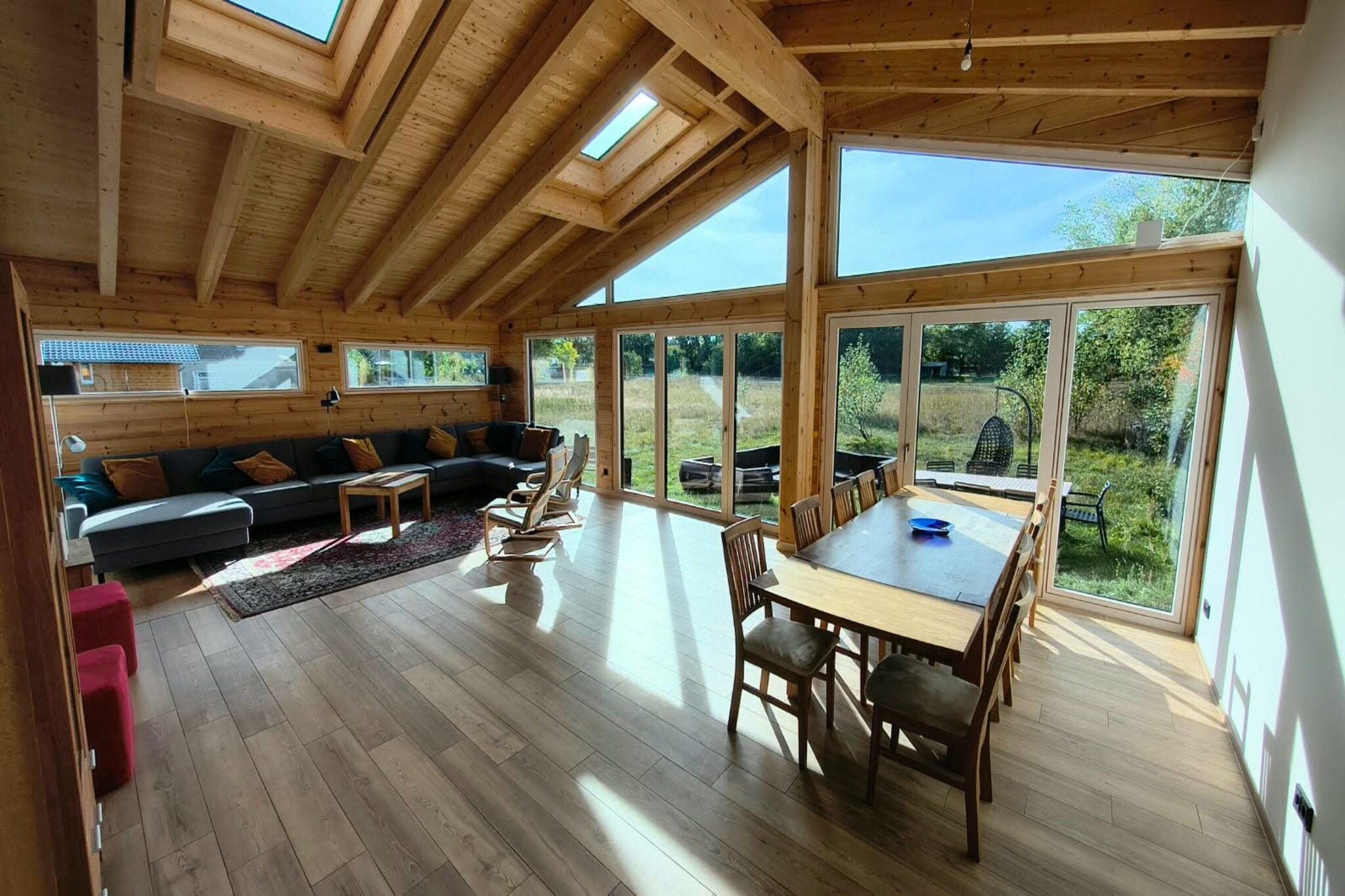 Une pièce spacieuse avec un plafond en bois, de grandes fenêtres, un canapé, une table à manger et des chaises.