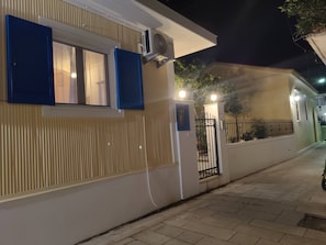 Un edifici amb façana blanca, una finestra amb persianes blaves i un aparell d'aire condicionat fixat a la paret.