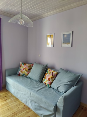 A room with a light blue sofa, two colorful pillows, a white pendant light, and two framed pictures on the wall. - 4-bedroom house with a garden in the center of Lefkada (Λευκάδα)