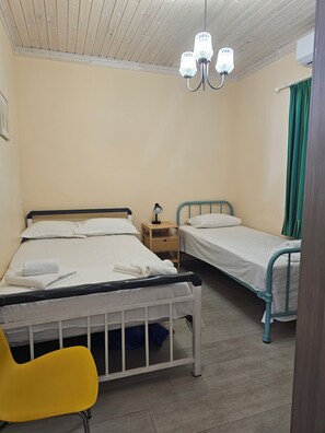 A bedroom with two single beds, a bedside table with a lamp, a chair, and a ceiling light fixture. - 4-bedroom house with a garden in the center of Lefkada (Λευκάδα)