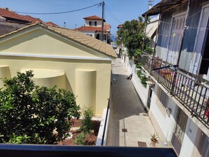 Un carrer estret amb edificis a ambdós costats, una petita zona de jardí i un cel serè.