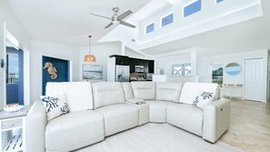 A spacious living room with a large L-shaped sectional sofa, a ceiling fan, and a view of the kitchen through an open doorway. - Ponce Paradise Oceanfront Home (Ponce Inlet)