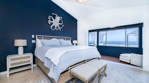 A bedroom with a bed, nightstands, a bench, and a view of the ocean. - Ponce Paradise Oceanfront Home (Ponce Inlet)