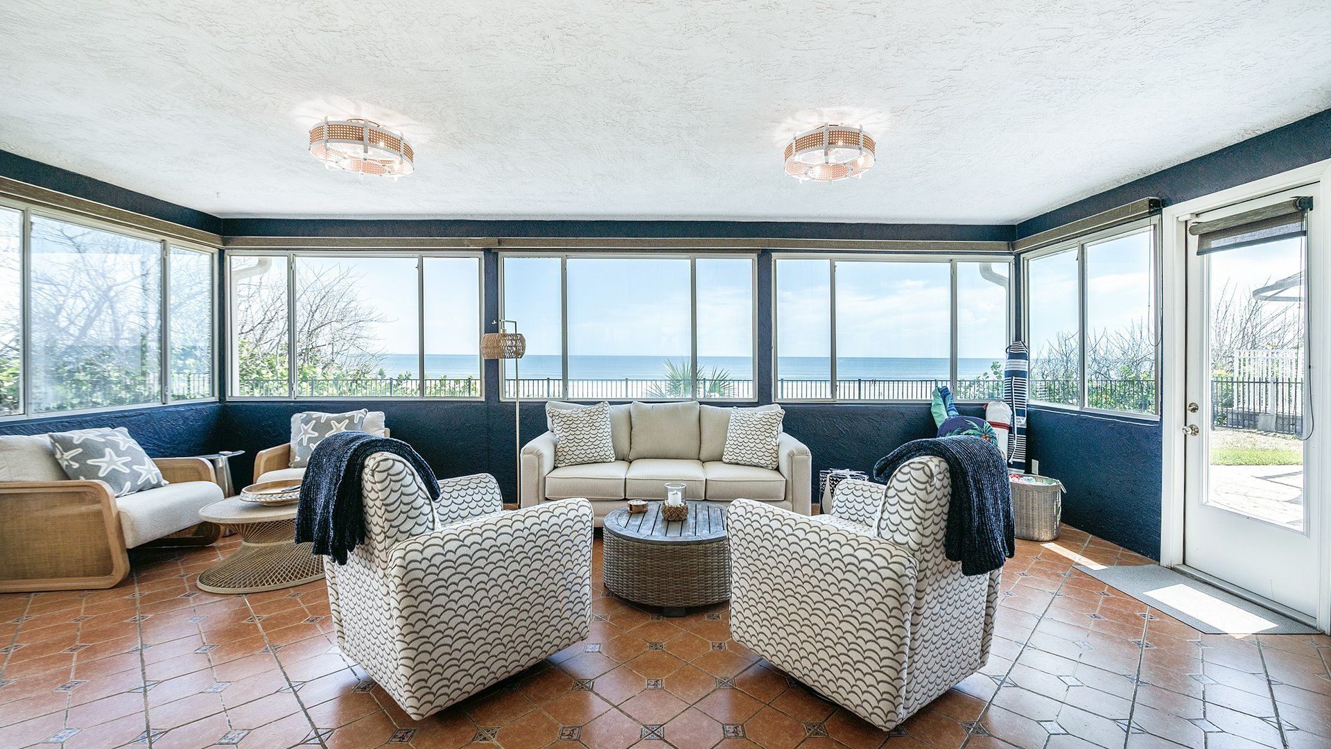 A sunroom with a view of the sea, furnished with a sofa, chairs, and a coffee table.